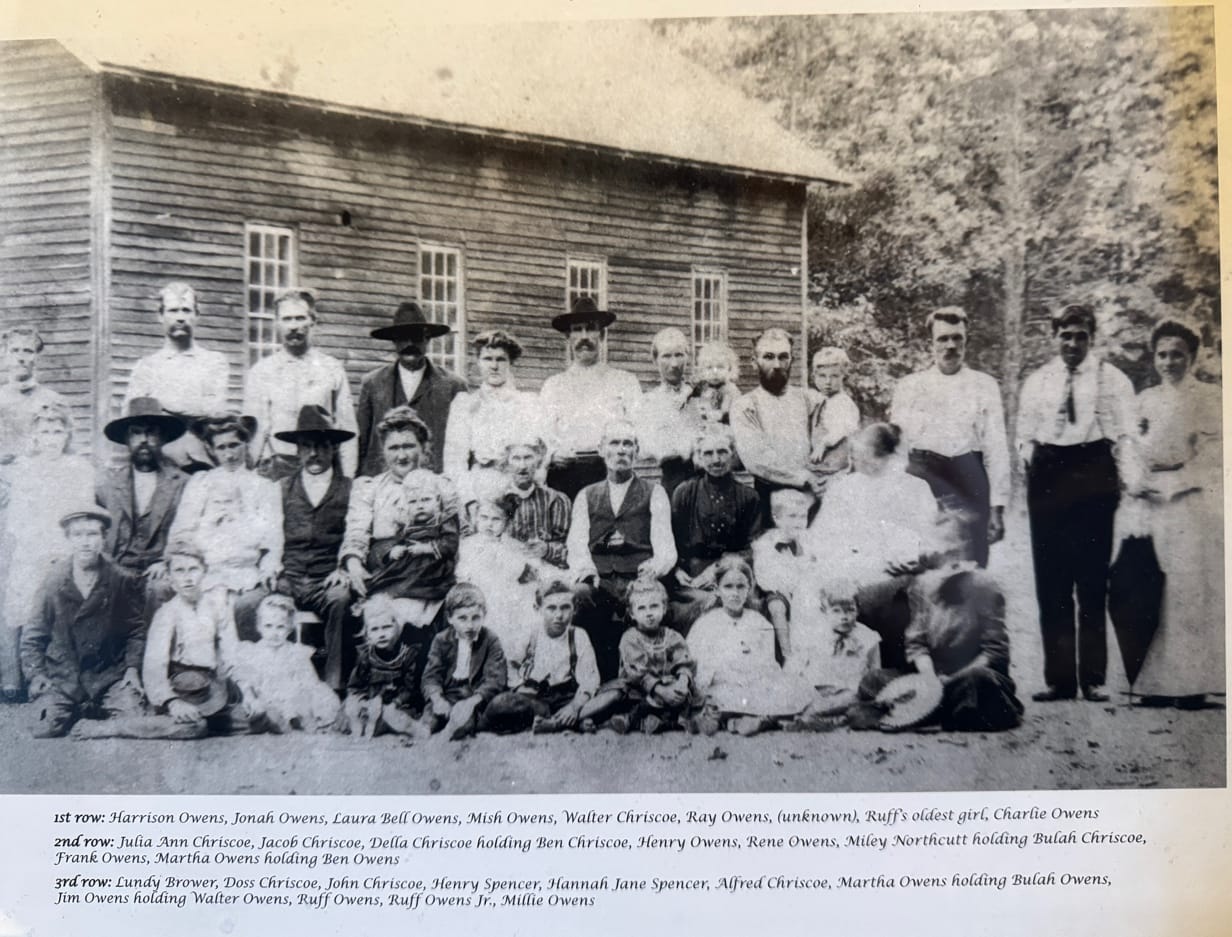 Owens family and community members gathered outside a wooden building, 1906